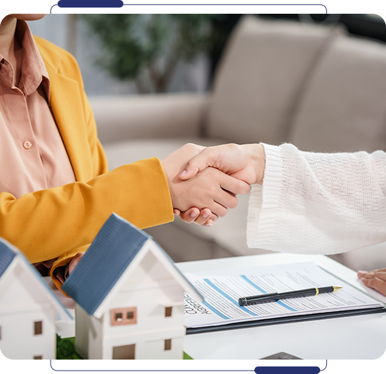 Two people shaking hands over a table with some houses.