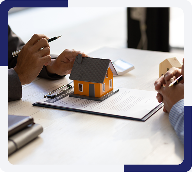 Two people are sitting at a table with paperwork and a model house.