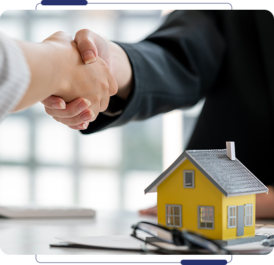Two people shaking hands over a table with a house.